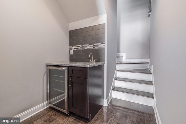 staircase with beverage cooler, wood finished floors, baseboards, vaulted ceiling, and indoor wet bar