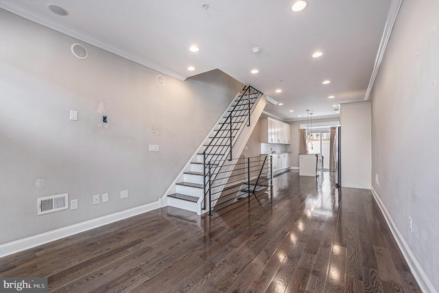 unfurnished living room featuring visible vents, baseboards, stairway, dark wood finished floors, and crown molding