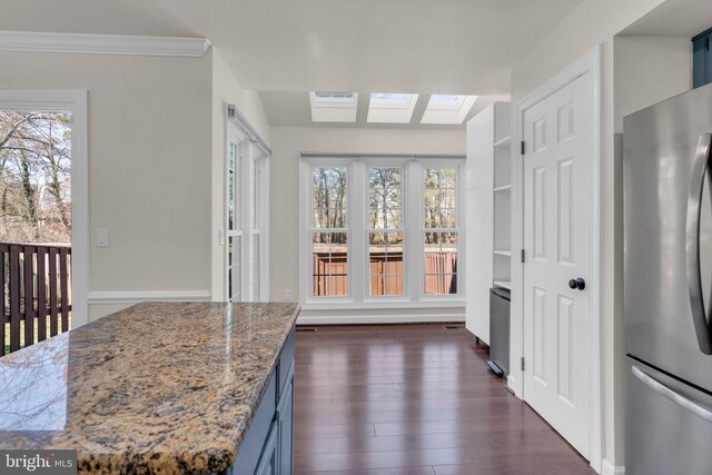 kitchen featuring dark wood-type flooring, blue cabinetry, freestanding refrigerator, a skylight, and light stone countertops