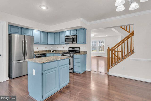 kitchen with blue cabinetry, a kitchen island, ornamental molding, appliances with stainless steel finishes, and dark wood-style flooring