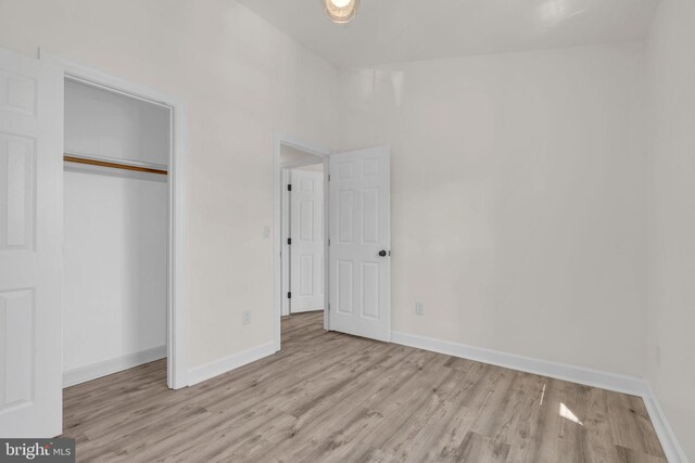 unfurnished bedroom with wood finished floors, baseboards, and a closet