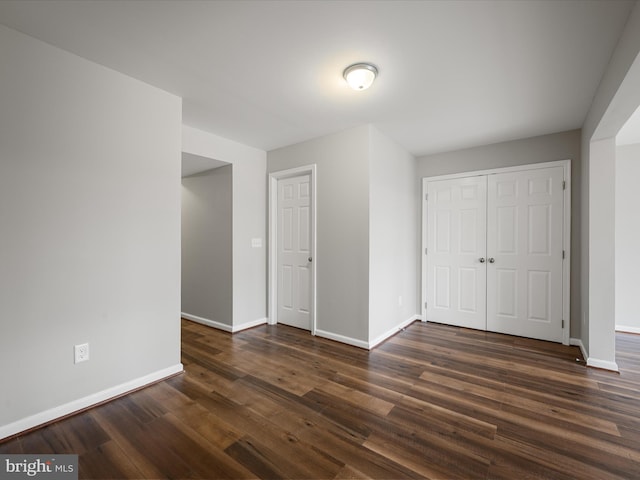 unfurnished bedroom with dark wood-type flooring, a closet, and baseboards