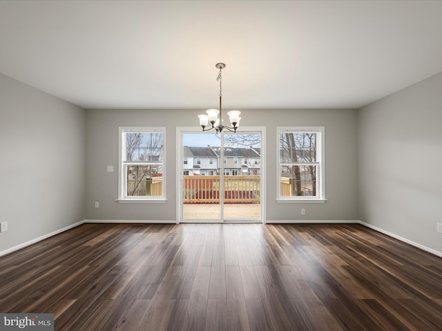 unfurnished dining area with baseboards, an inviting chandelier, dark wood finished floors, and a healthy amount of sunlight