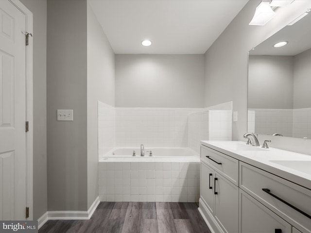 full bath with double vanity, a sink, wood finished floors, baseboards, and a bath