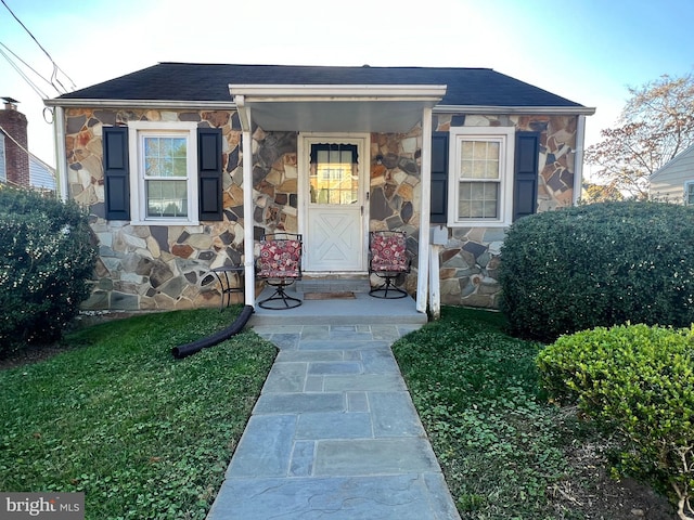 doorway to property with stone siding and roof with shingles