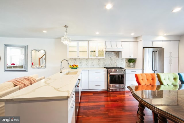 kitchen featuring a peninsula, premium range hood, a sink, appliances with stainless steel finishes, and decorative backsplash