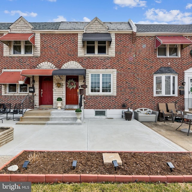 view of property with a high end roof, brick siding, and a patio