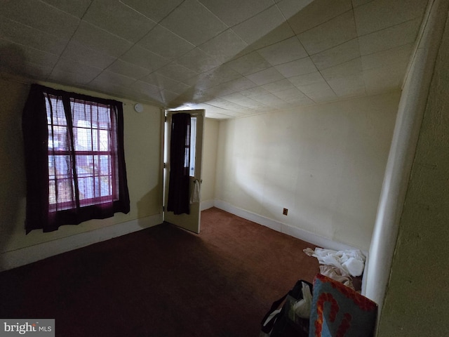 empty room featuring baseboards and dark colored carpet