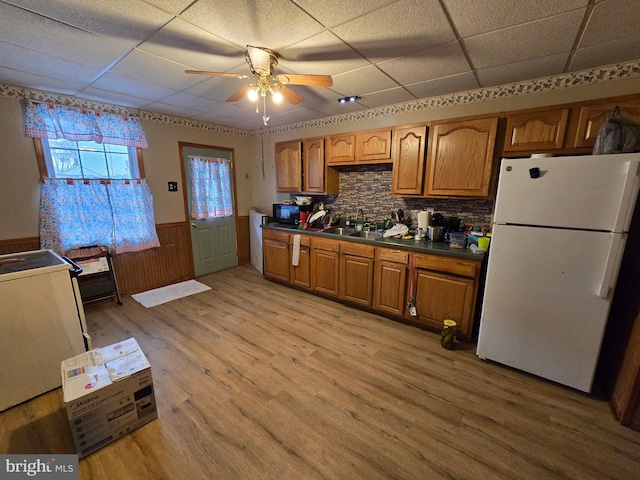 kitchen with light wood-style flooring, a wainscoted wall, freestanding refrigerator, brown cabinets, and dark countertops