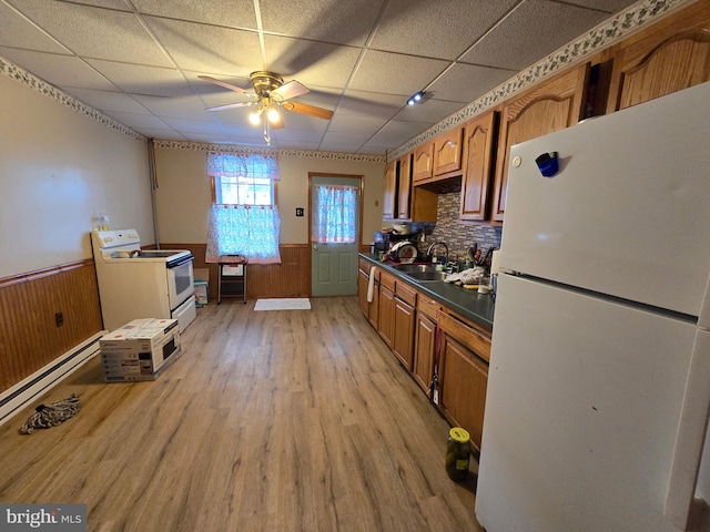 kitchen featuring dark countertops, white appliances, a wainscoted wall, and a sink