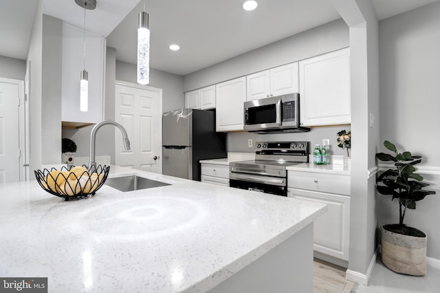 kitchen featuring light stone countertops, a sink, stainless steel appliances, white cabinets, and pendant lighting