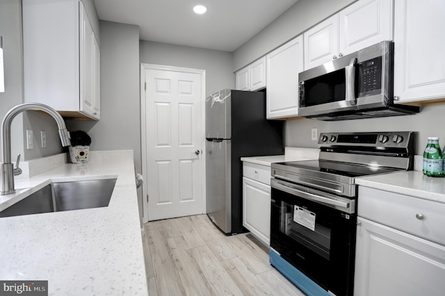 kitchen with light wood finished floors, white cabinetry, stainless steel appliances, and a sink