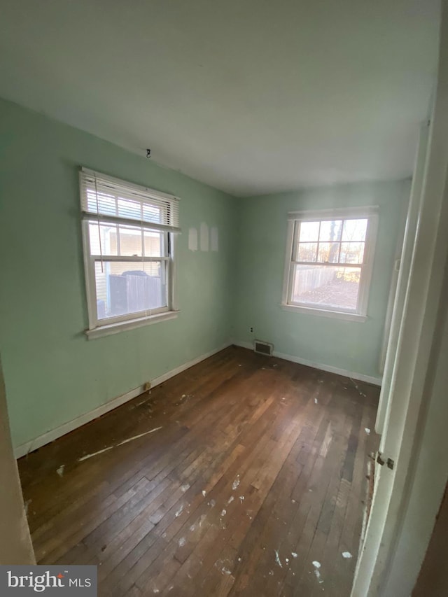 unfurnished room featuring a wealth of natural light, visible vents, baseboards, and hardwood / wood-style flooring