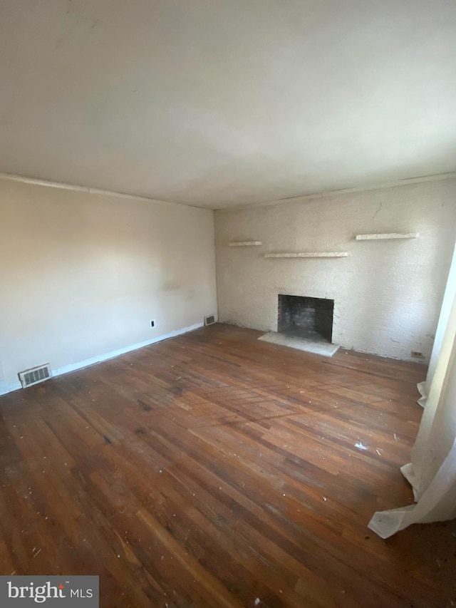 unfurnished living room featuring hardwood / wood-style flooring, a brick fireplace, and visible vents