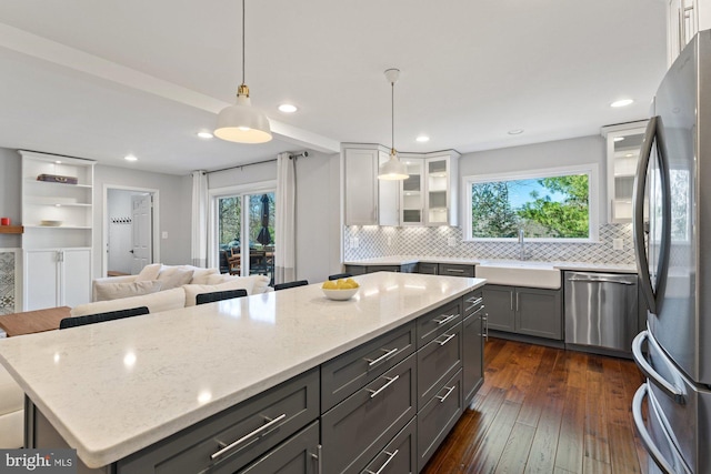 kitchen with light stone counters, dark wood-style flooring, stainless steel appliances, a sink, and a kitchen island