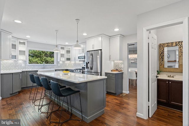 kitchen with a breakfast bar, dark wood-style flooring, light countertops, appliances with stainless steel finishes, and glass insert cabinets