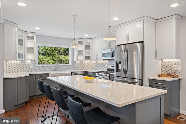 kitchen with stainless steel appliances, a breakfast bar area, gray cabinets, and light stone countertops