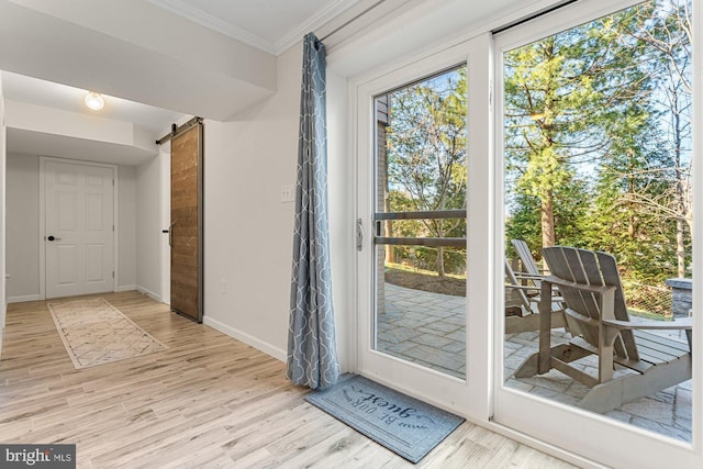 doorway to outside with light wood-type flooring, a barn door, baseboards, and crown molding