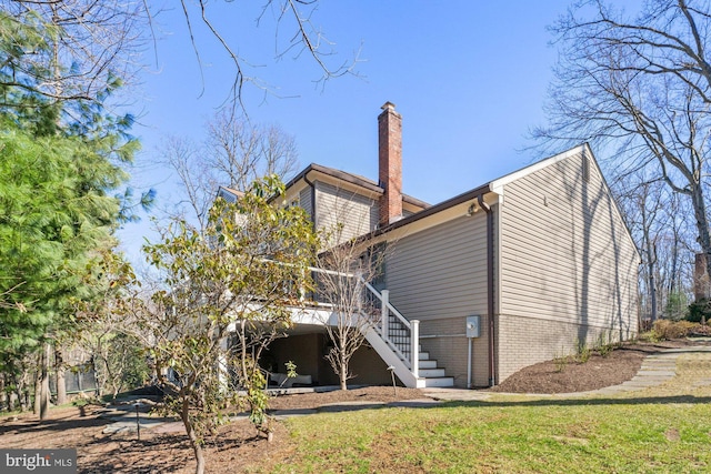 rear view of house with brick siding, a yard, a chimney, and stairs