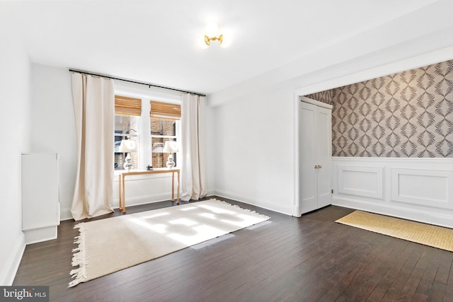 spare room with dark wood-style flooring, wainscoting, and wallpapered walls