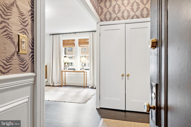 interior space with wallpapered walls, dark wood-type flooring, and wainscoting