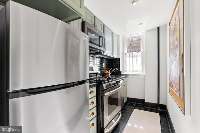 kitchen with decorative backsplash, green cabinets, appliances with stainless steel finishes, dark tile patterned floors, and baseboards