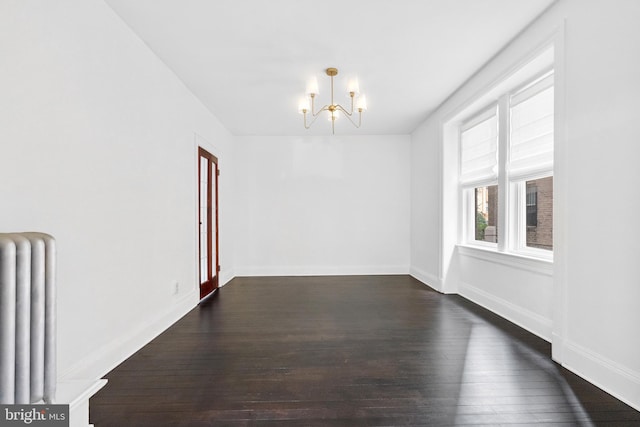 empty room with a notable chandelier, baseboards, dark wood finished floors, and radiator