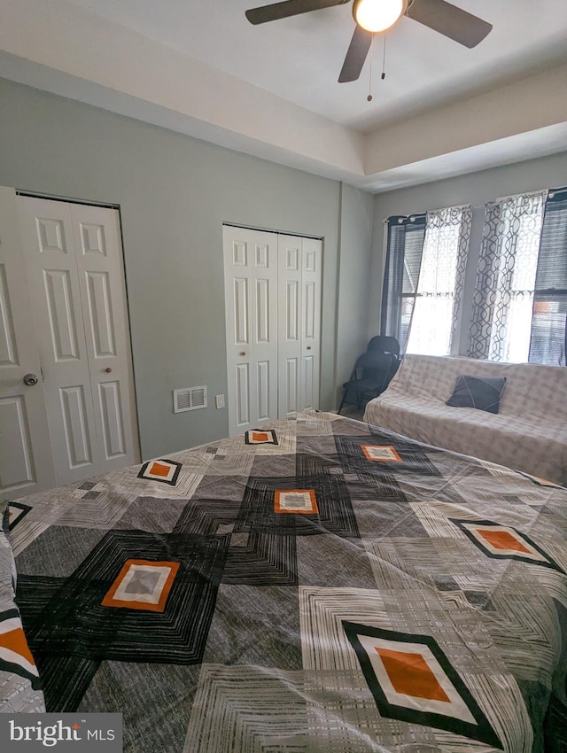 bedroom featuring a ceiling fan, visible vents, carpet floors, and multiple closets