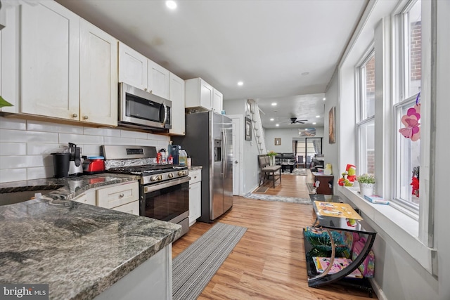 kitchen featuring a ceiling fan, light wood-style floors, appliances with stainless steel finishes, white cabinetry, and backsplash