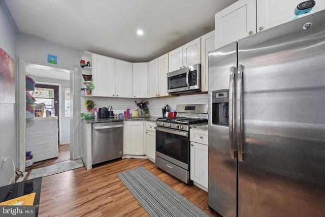 kitchen featuring dark stone countertops, backsplash, white cabinetry, stainless steel appliances, and light wood finished floors