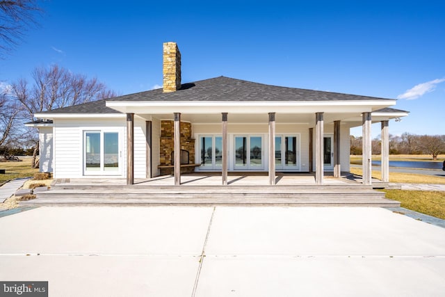 back of property with a shingled roof, french doors, and a chimney