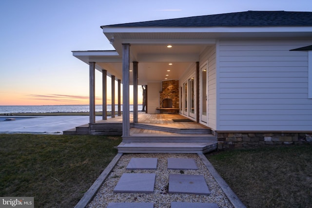 view of exterior entry featuring a yard, a shingled roof, and a water view