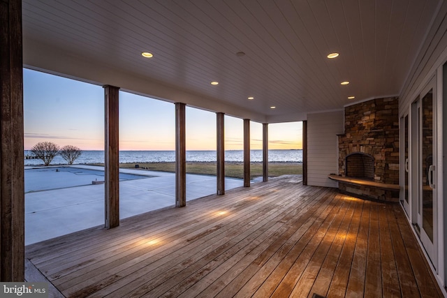 unfurnished sunroom featuring wood ceiling, a view of the beach, an outdoor stone fireplace, and a water view