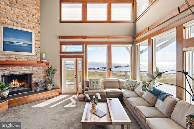 living area featuring a water view, a towering ceiling, carpet flooring, and a stone fireplace