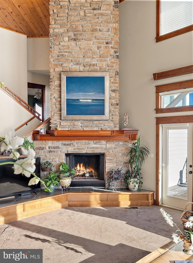 living area featuring wooden ceiling, a stone fireplace, and a high ceiling