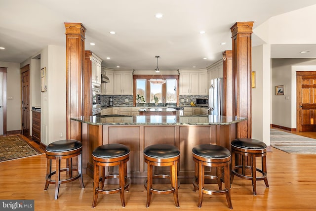 kitchen featuring appliances with stainless steel finishes, dark stone countertops, backsplash, and decorative columns