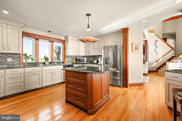 kitchen with a sink, light wood-style floors, stainless steel refrigerator with ice dispenser, decorative backsplash, and dark stone countertops