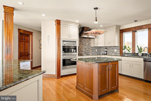 kitchen featuring stainless steel appliances, dark stone counters, light wood finished floors, and custom exhaust hood