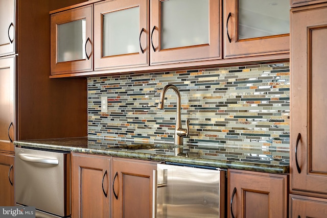 kitchen featuring brown cabinets, dishwasher, tasteful backsplash, dark countertops, and glass insert cabinets