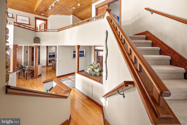 stairway with wooden ceiling, a high ceiling, wood finished floors, visible vents, and decorative columns