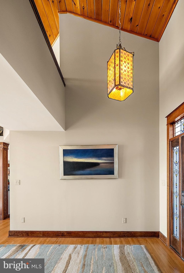 entryway with a high ceiling, wooden ceiling, wood finished floors, and baseboards