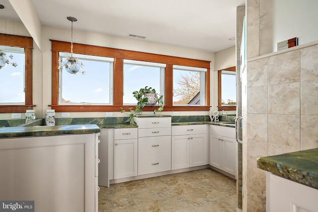 kitchen featuring pendant lighting, tile walls, visible vents, white cabinets, and dark stone counters