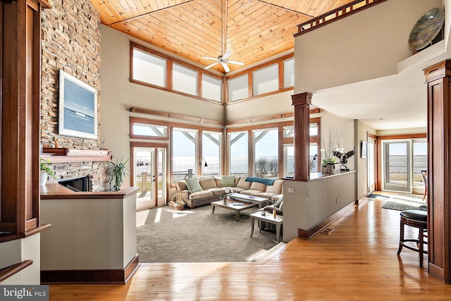 living room with a stone fireplace, a high ceiling, wood finished floors, and decorative columns