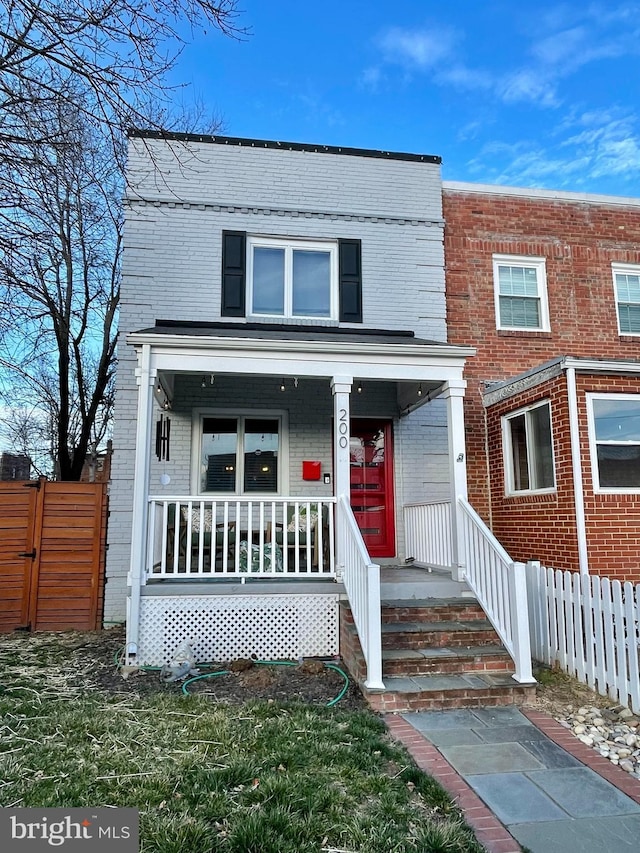 view of property featuring a porch, brick siding, and fence