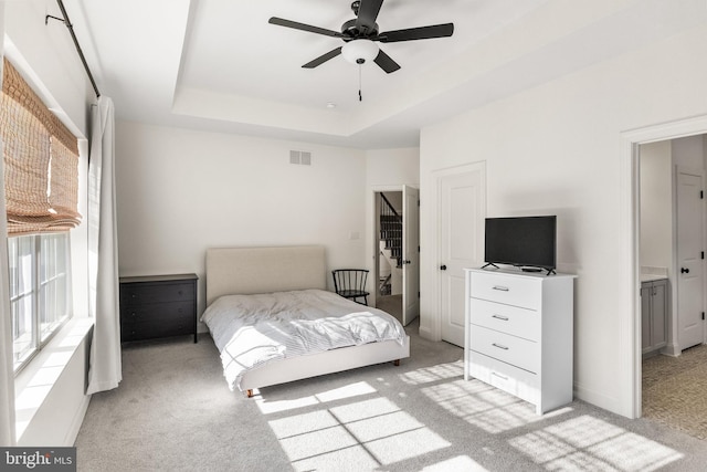 bedroom with light colored carpet, a tray ceiling, visible vents, and baseboards