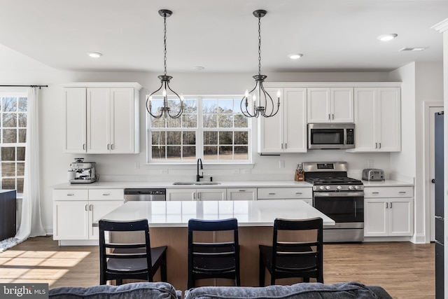 kitchen featuring appliances with stainless steel finishes, a breakfast bar, wood finished floors, light countertops, and a sink