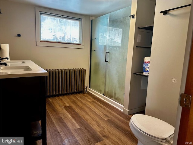 bathroom featuring toilet, radiator heating unit, a stall shower, a sink, and wood finished floors