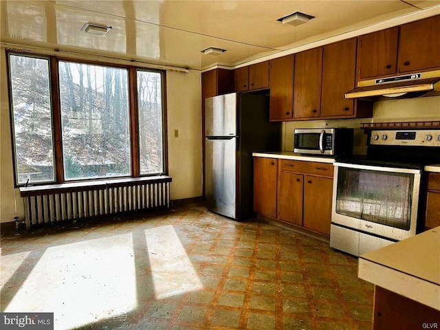 kitchen featuring radiator heating unit, appliances with stainless steel finishes, tile patterned floors, light countertops, and under cabinet range hood