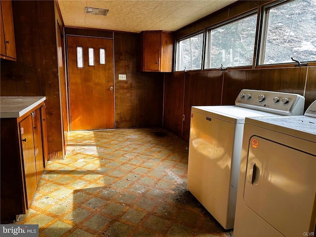 washroom with light floors, separate washer and dryer, wood walls, and cabinet space