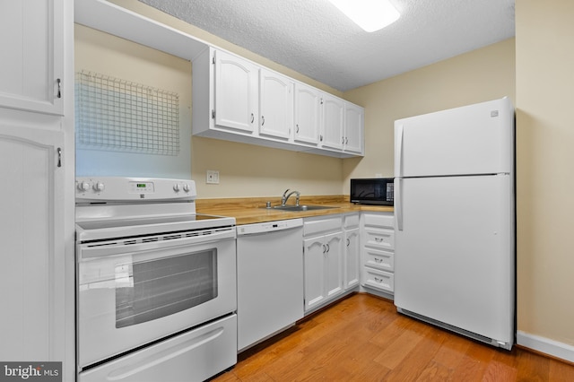 kitchen with a sink, white appliances, light wood-style floors, and white cabinets